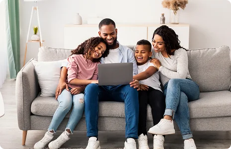 Happy family sitting on a couch, smiling and laughing together while looking at a laptop in their living room