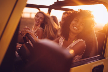 Smiling Afro girl with girl friends on a summer vacation road trip at sunset