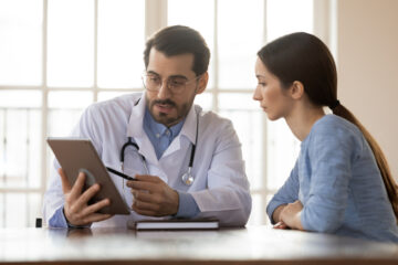 young woman with doctor looking at insurance info on tablet