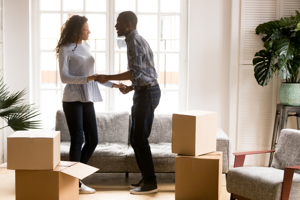 Young African American couple holding hands in the living room of their apartment with boxes around them